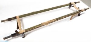 Drewniane nosze ze szpitala obozowego. Drewniana konstrukcja pomalowana farbą w kolorze zielonym, z dwóch stron doczepione metalowe okucia. Nosze bardzo zniszczone, zachowane jedynie fragmenty doczepionego brezentu w kolorze białym.